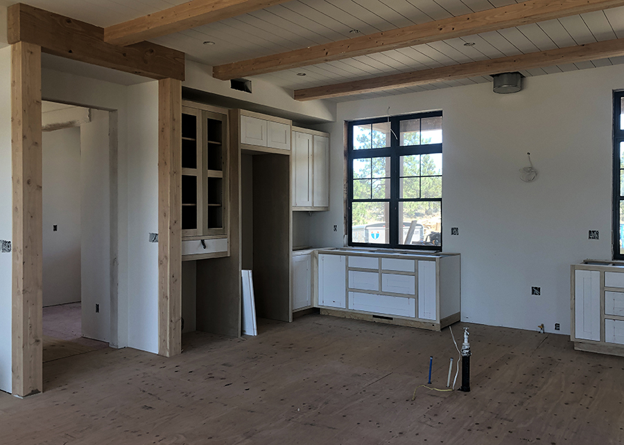 Early construction of the modern country kitchen - sub flooring ready for hardwood covering, and custom wooden cabinetry can be seen below the paneled ceiling featuring exposed beams